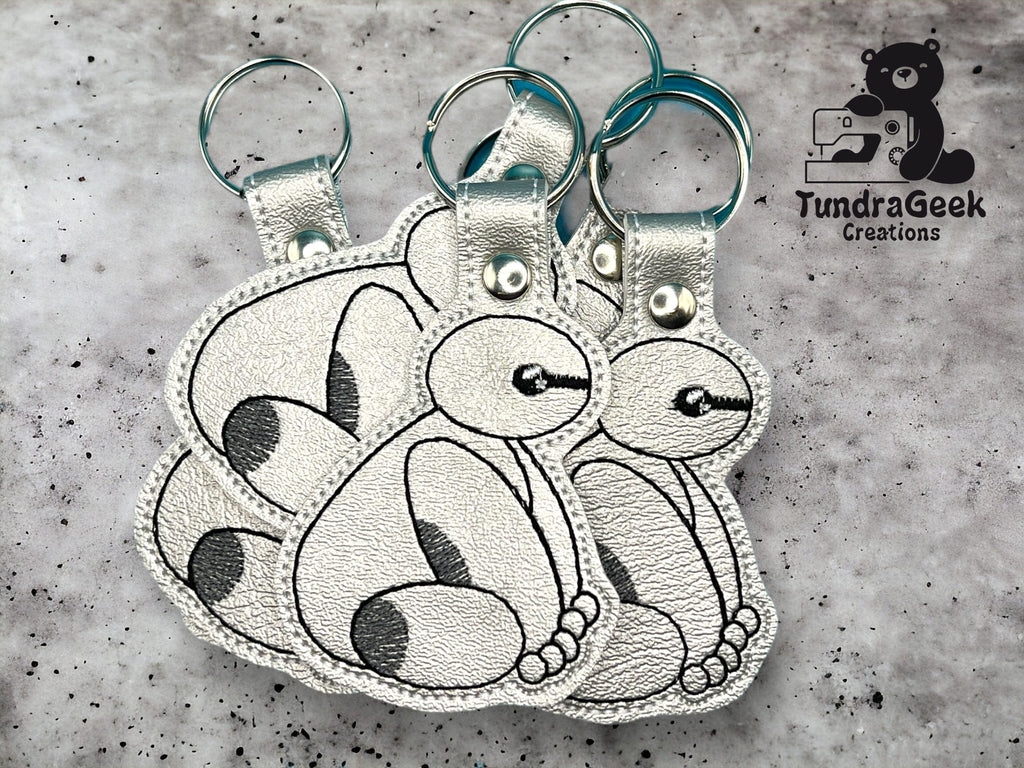 Three silver keychains with stitched cartoon-style animal designs are displayed on a gray surface next to the TundraGeek Creations logo.