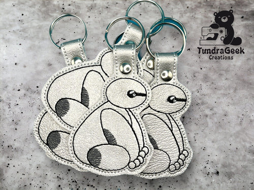 Three silver keychains with stitched cartoon-style animal designs are displayed on a gray surface next to the TundraGeek Creations logo.