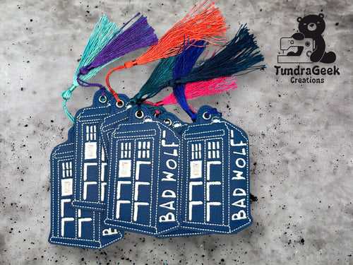 Four blue embroidered keychains shaped like a TARDIS with BAD WOLF text and colorful tassels, set on a gray background with the TundraGeek Creations logo.