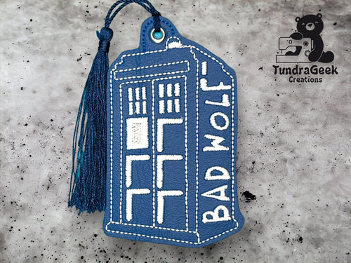 A blue, rectangular keychain shaped like the TARDIS from Doctor Who, embroidered with the words BAD WOLF and a blue tassel attached. TundraGeek Creations logo in the corner.