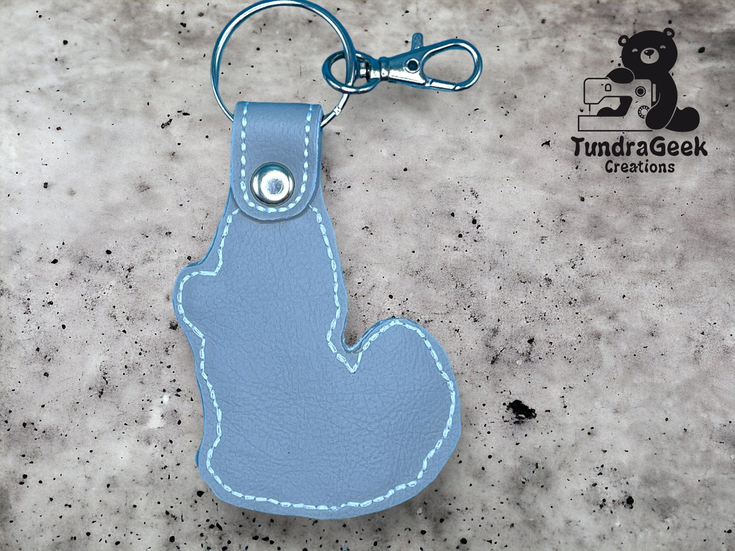 Light blue leather keychain in the shape of a squirrel, attached to a metal keyring and clasp, with the TundraGeek Creations logo in the background.