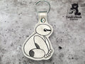 A keychain featuring a stitched outline of a sitting robot character on metallic silver material, displayed on a textured gray background with the TundraGeek Creations logo.