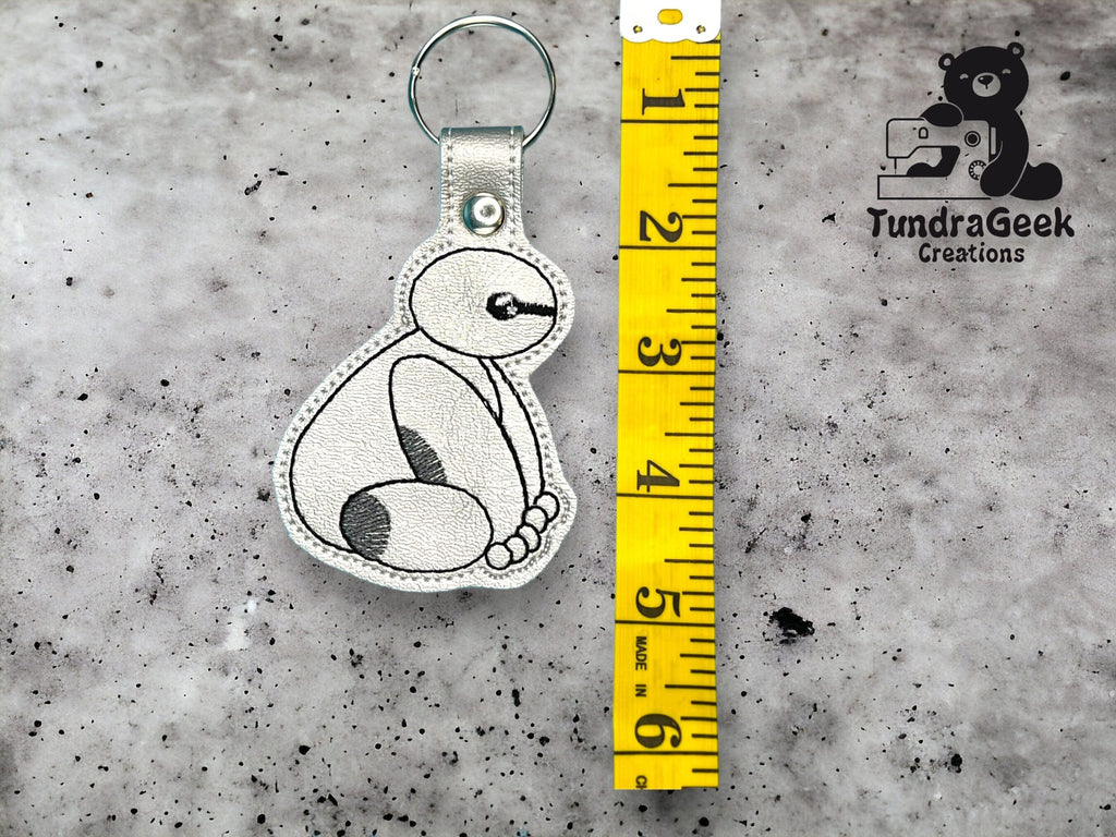 A white embroidered sloth keychain sits next to a yellow measuring tape showing it is about 4 inches tall; “TundraGeek Creations” logo is in the top right corner.