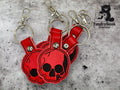 Three red faux leather skull keychains with metal rings and clips are arranged on a textured surface. A TundraGeek Creations logo appears in the upper right corner.