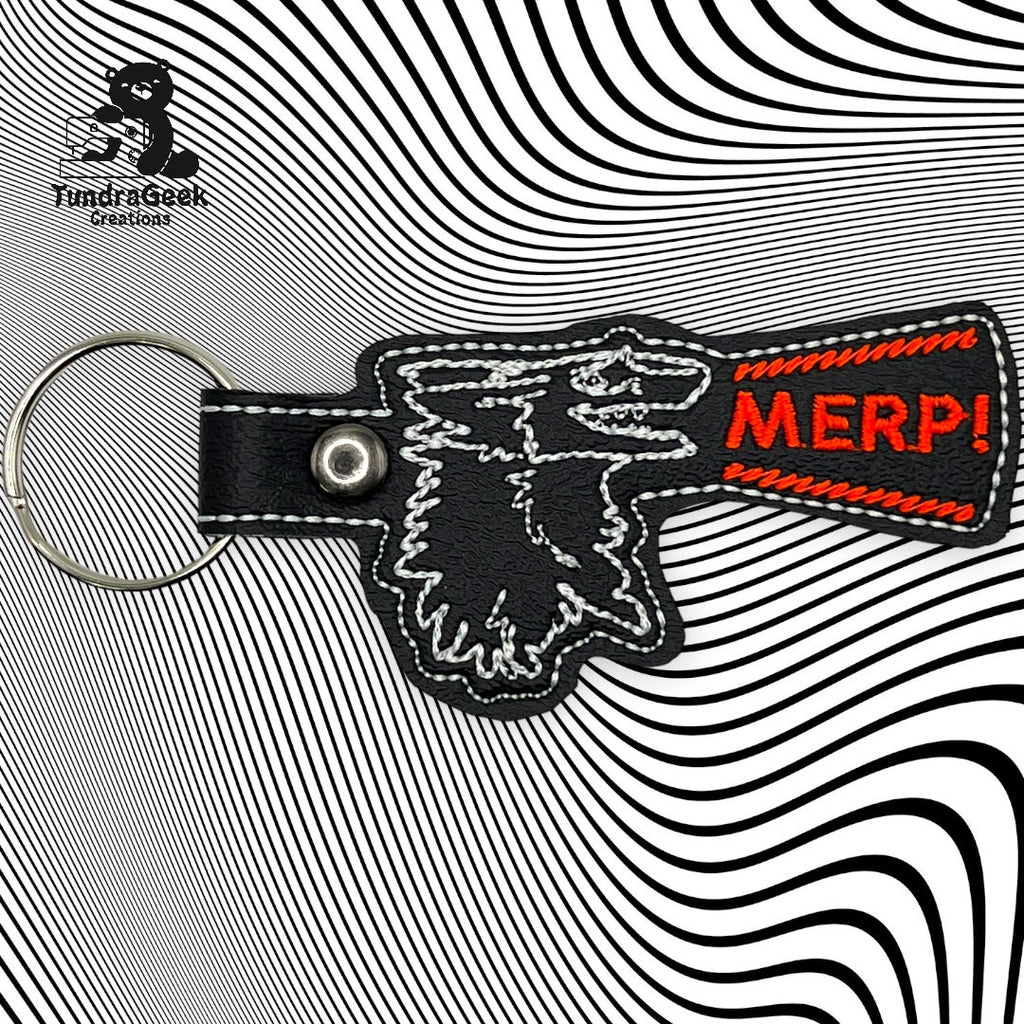 Keychain with stitched outline of a wolfs head and a red patch reading MERP! on a wavy black and white background. FundiGeek Creations logo in top left corner.