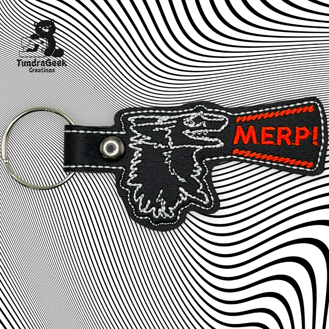 Keychain with stitched outline of a wolfs head and a red patch reading MERP! on a wavy black and white background. FundiGeek Creations logo in top left corner.