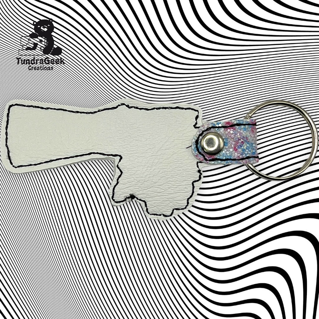 A keychain in the shape of Oklahoma with a metal ring and snap, placed on a black and white wavy patterned background. FundrisGeek Creations logo is in the top left corner.