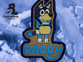 An embroidered patch of a cartoon blue dog wearing a backpack with the word DADDY below, displayed on a marbled blue background with the TundraGeek Creations logo.