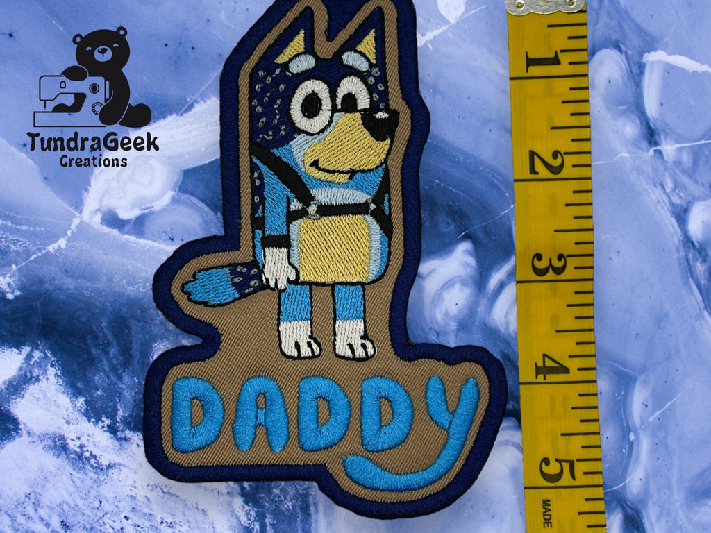 An embroidered patch featuring a cartoon dog above the word DADDY, next to a yellow measuring tape showing a length of about 4.5 inches.