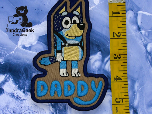 An embroidered patch featuring a cartoon dog above the word DADDY, next to a yellow measuring tape showing a length of about 4.5 inches.