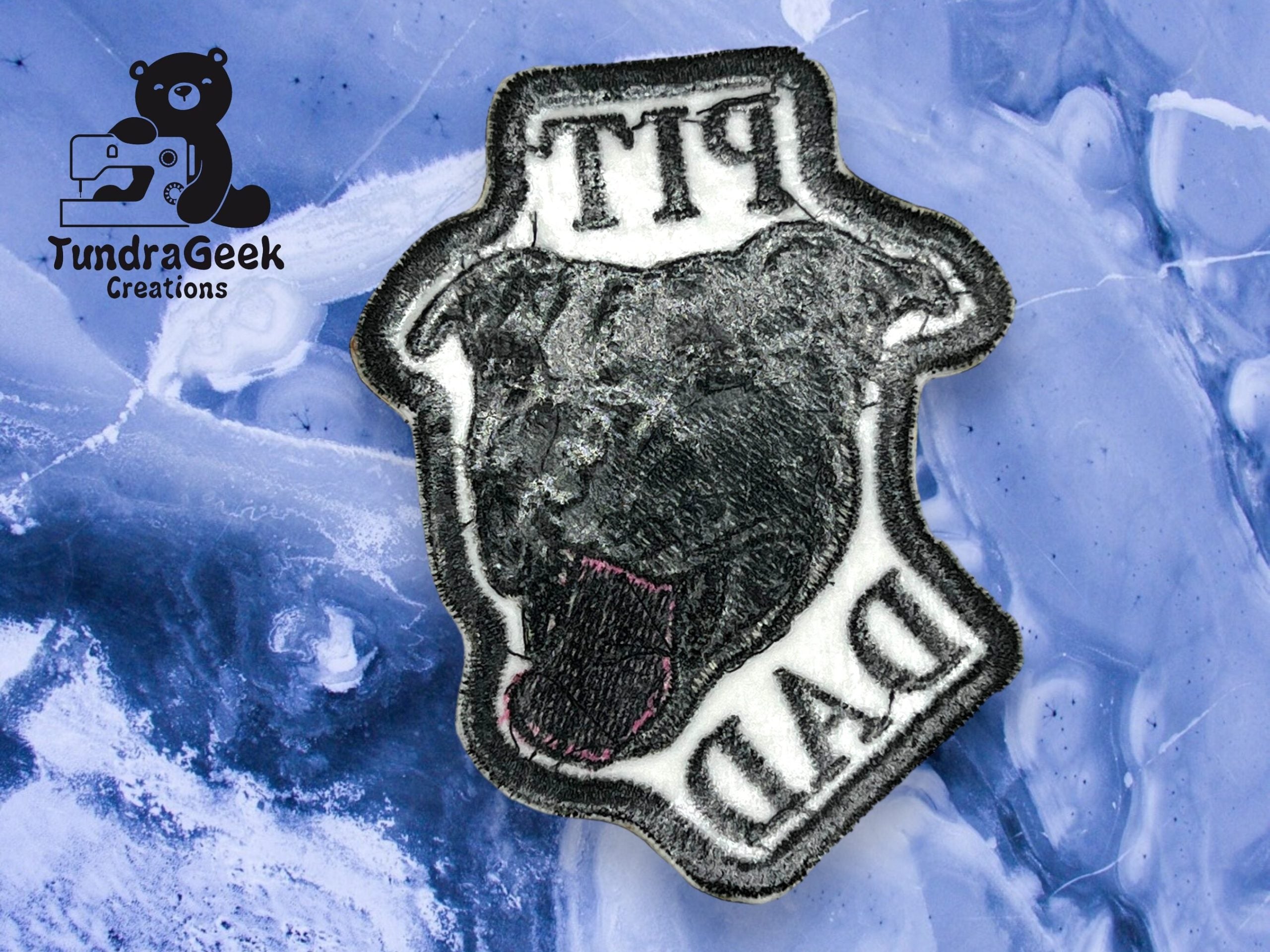 A patch showing a black dog’s head and the words “PIT DAD” on a marbled blue background with the “TundraGeek Creations” logo in the corner.