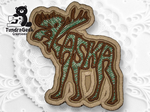 Embroidered patch of a moose with the word Alaska integrated into its body, placed on a decorative white background with the TundraGeek Creations logo in the corner.
