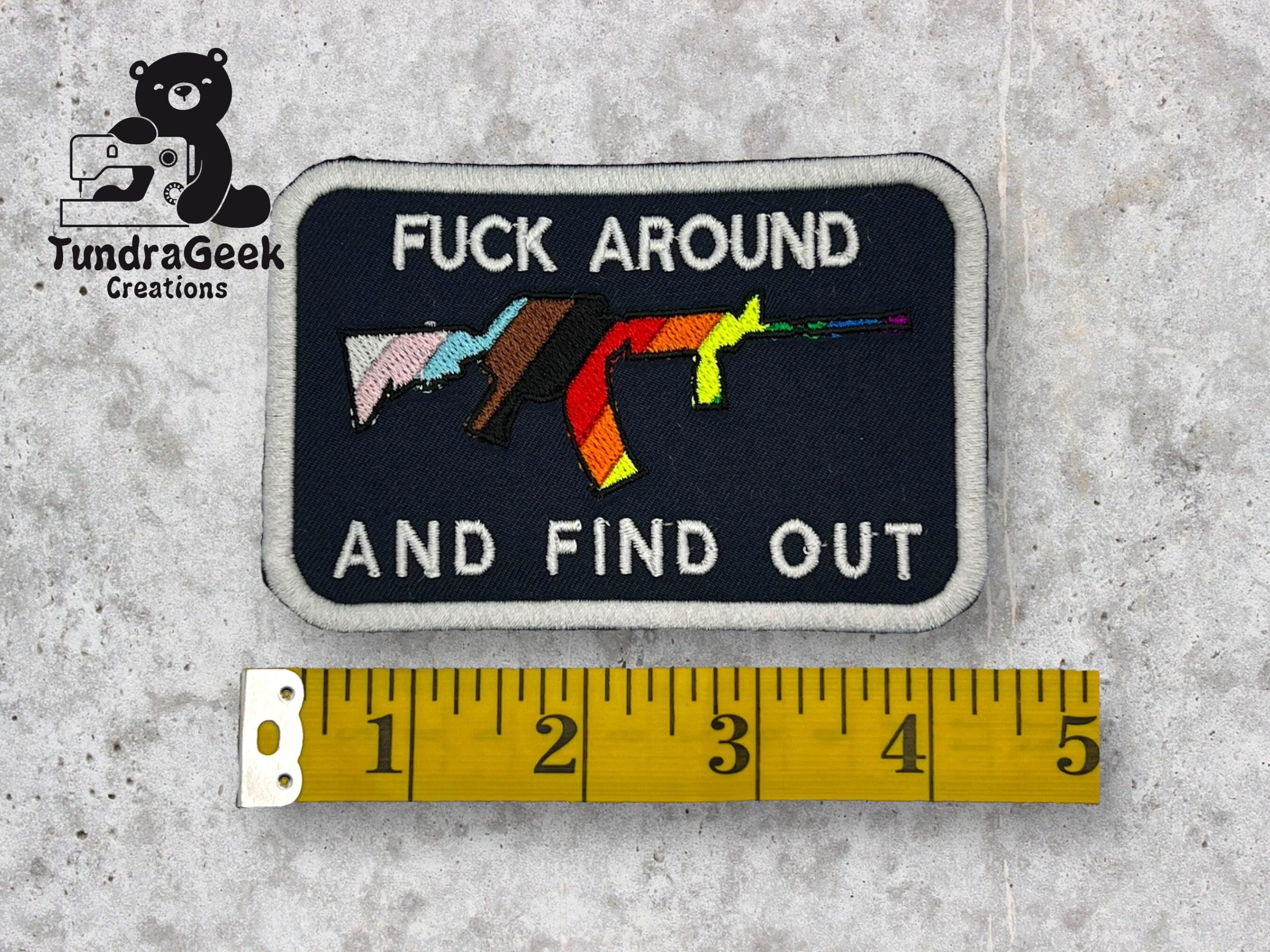 A rectangular patch with three rifles and the text FUCK AROUND AND FIND OUT, next to a yellow measuring tape showing a length of about 4 inches. TundraGeek Creations logo in the corner.