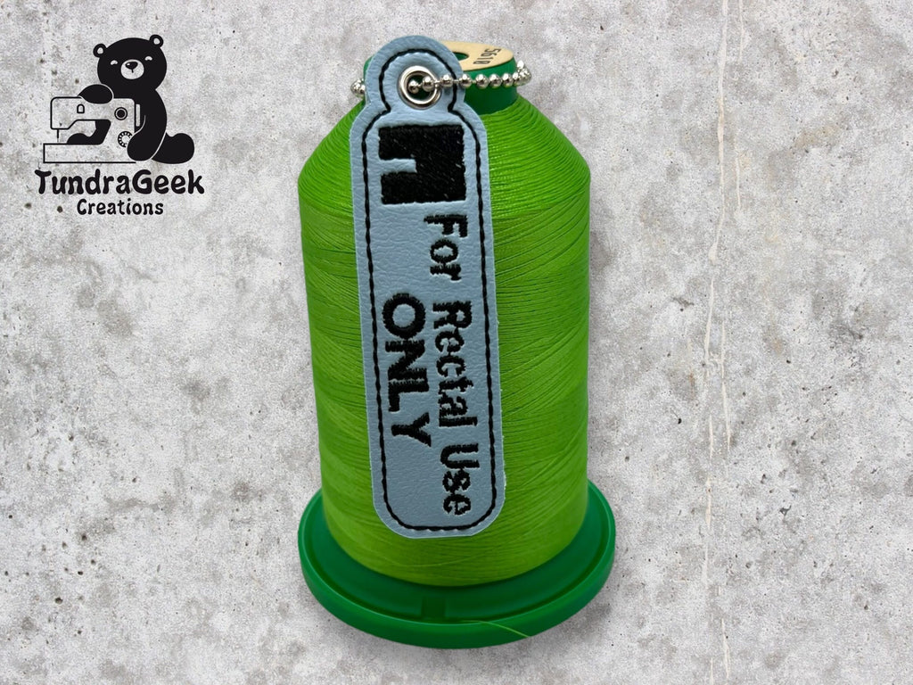A green spool of thread with a gray tag labeled For Rectal Use ONLY next to the TundraGeek Creations logo on a gray textured surface.