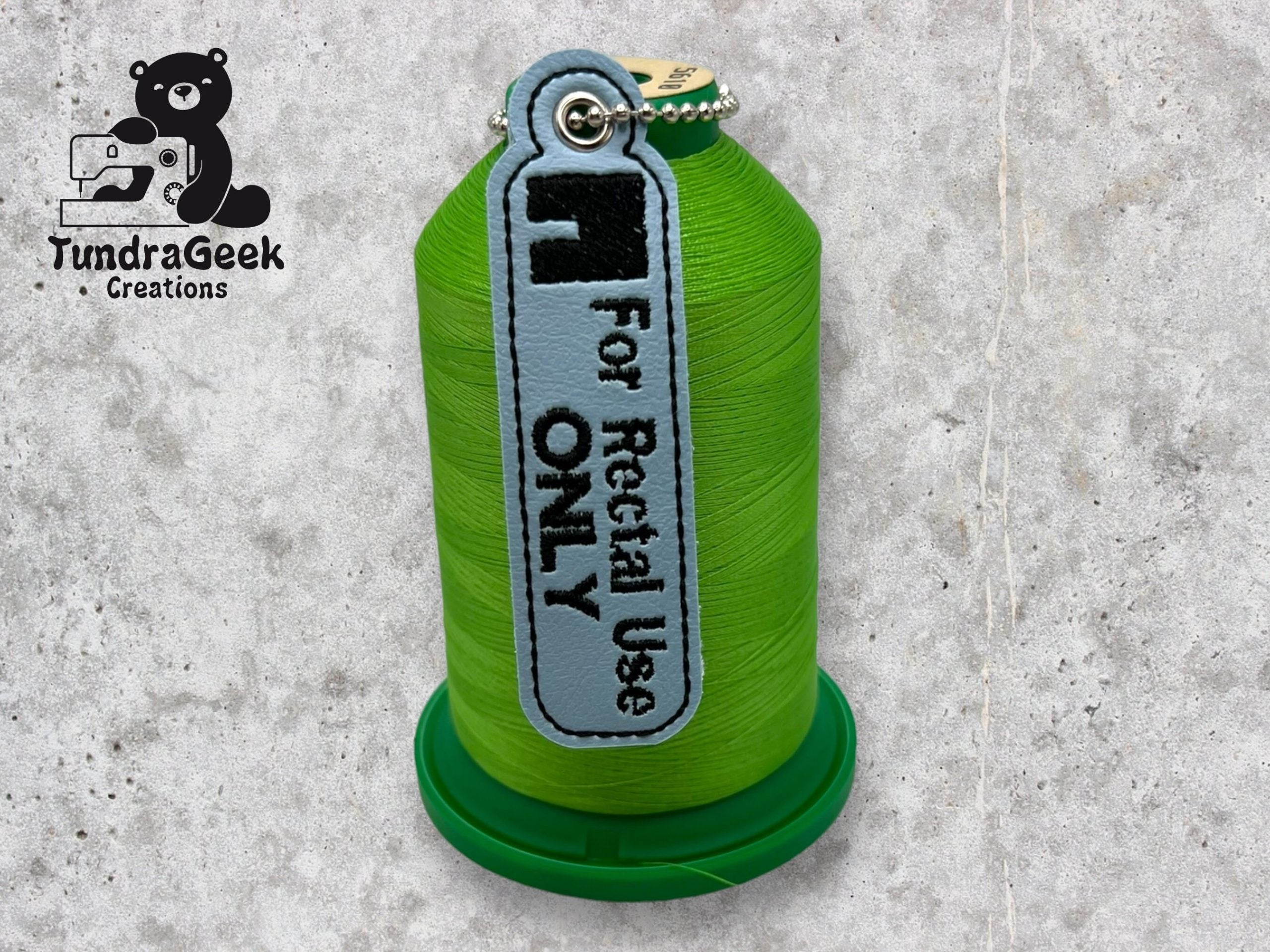 A green spool of thread with a gray tag labeled For Rectal Use ONLY next to the TundraGeek Creations logo on a gray textured surface.