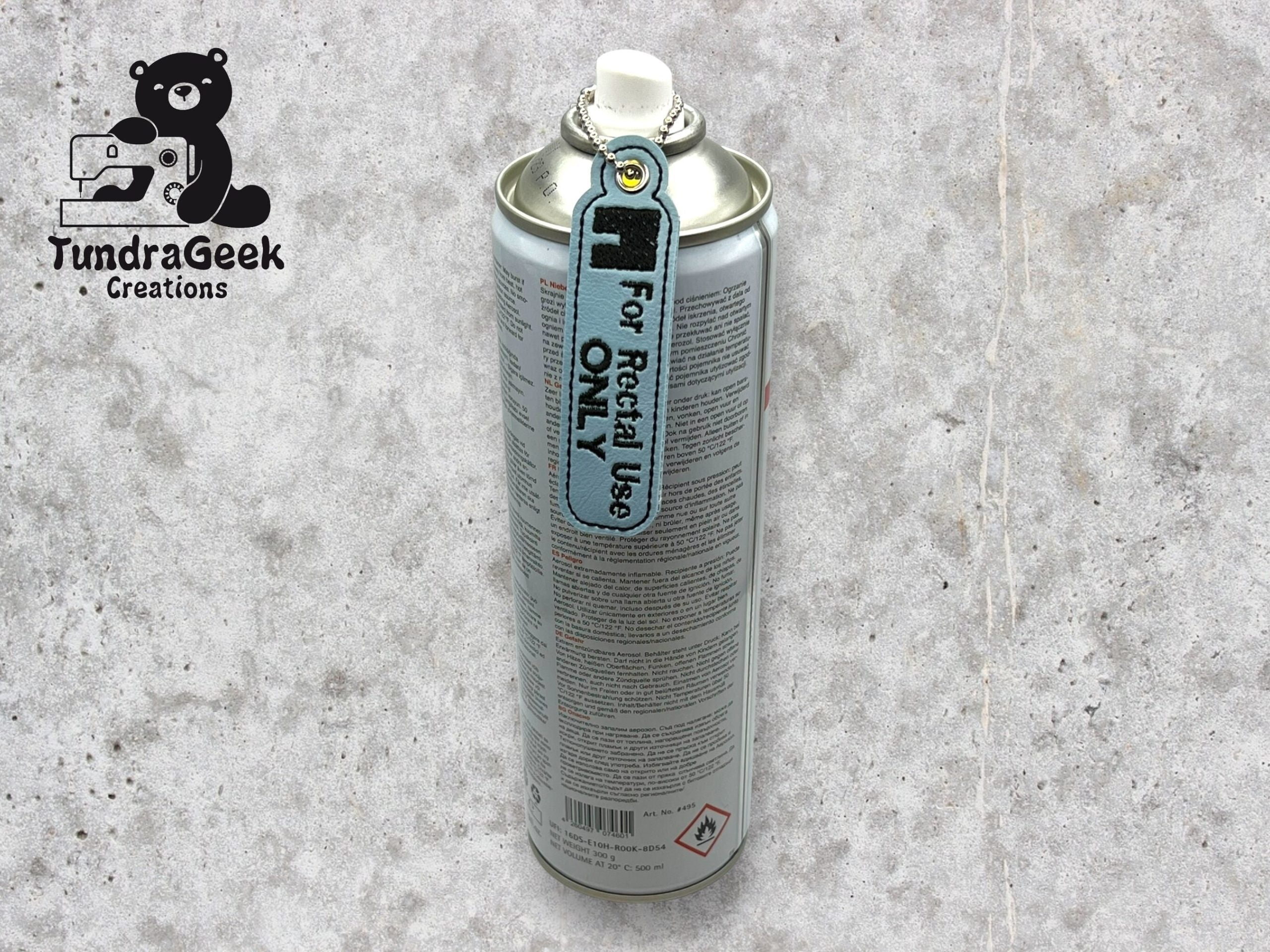 A spray can with a tag attached to the nozzle that reads For Recital Use Only stands upright on a light gray surface. The TundraGeek Creations logo appears in the top left corner.