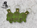 Three green, stitched Cthulhu keychains with metal rings are arranged on a gray textured surface. The TundraGeek Creations logo is in the top left corner.