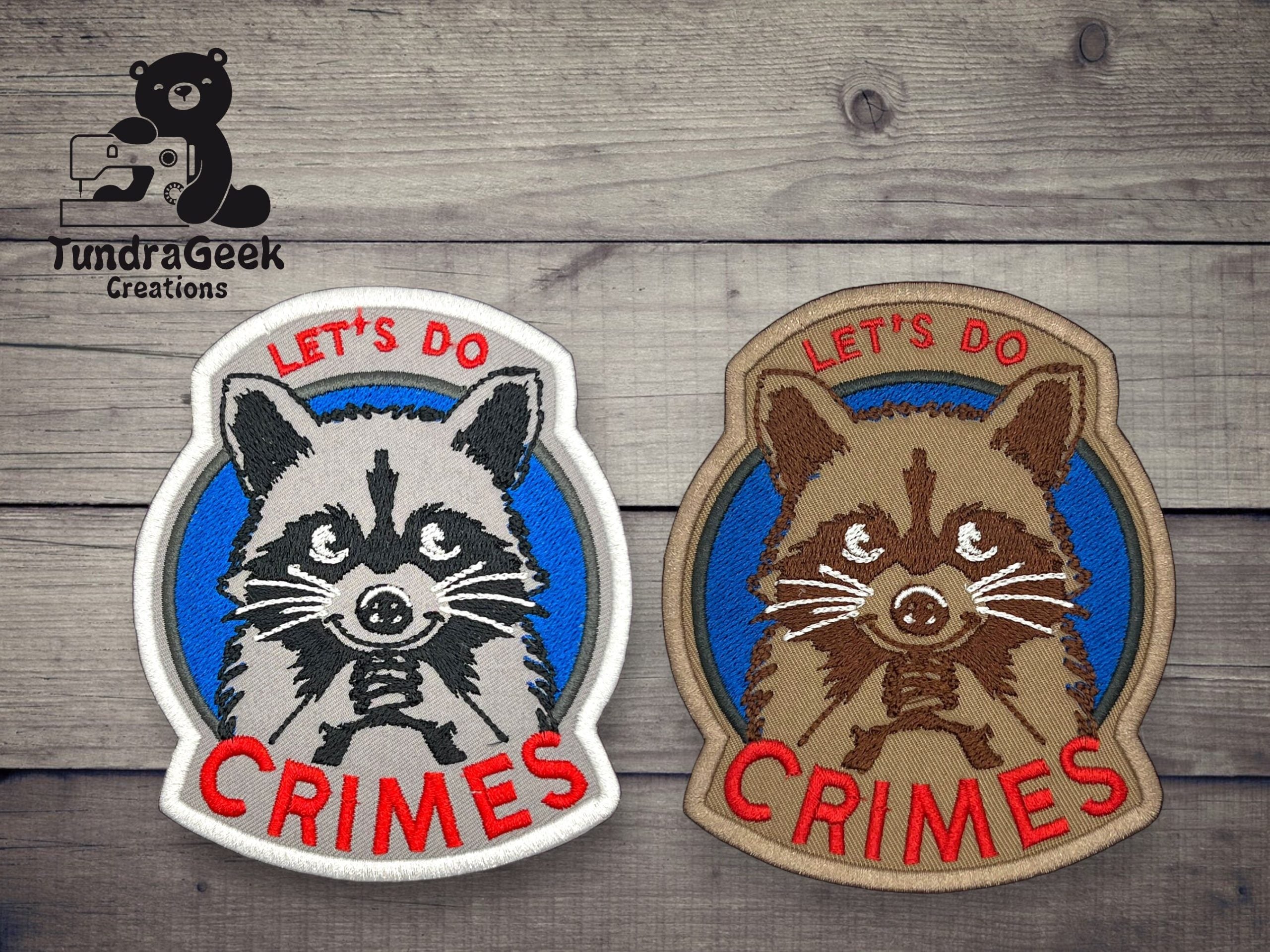 Two embroidered raccoon patches with the text LETS DO CRIMES are displayed on a wooden surface; one patch is white and blue, the other is brown and tan.