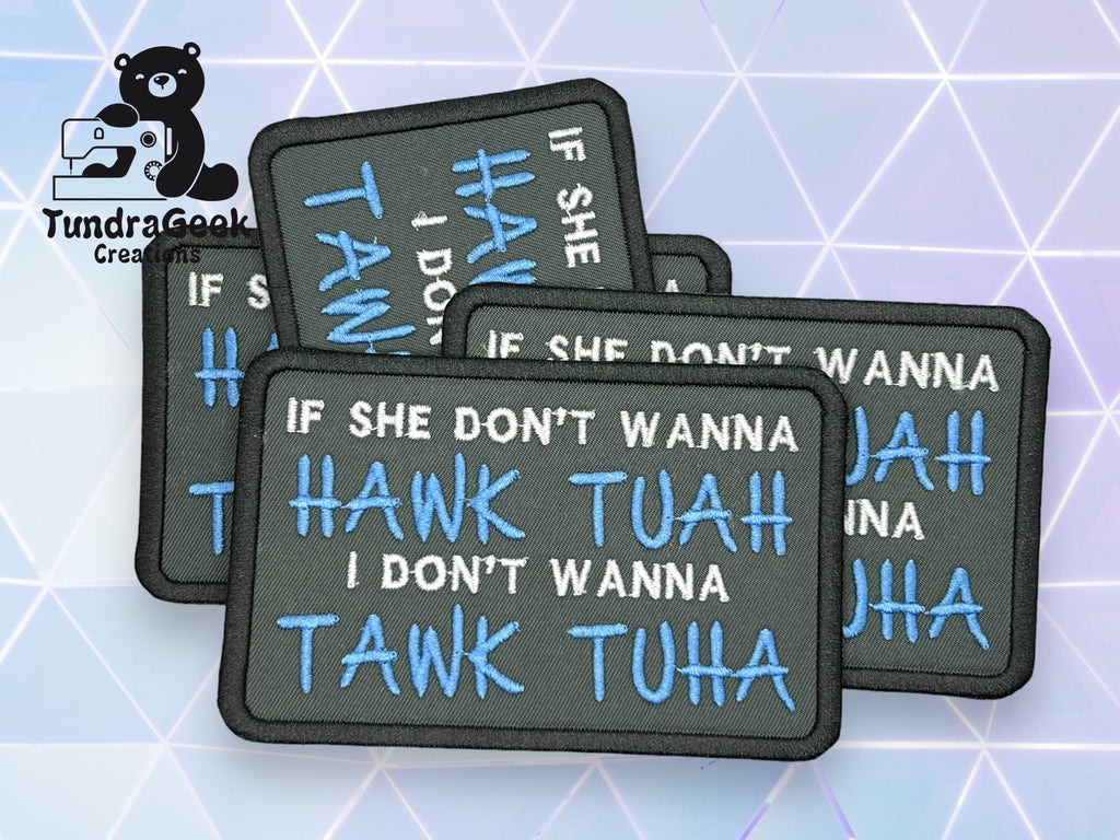 Four black rectangular patches with white and blue embroidered text read, IF SHE DONT WANNA HAWK TUAH I DONT WANNA TANK TUHA, arranged on a geometric background.