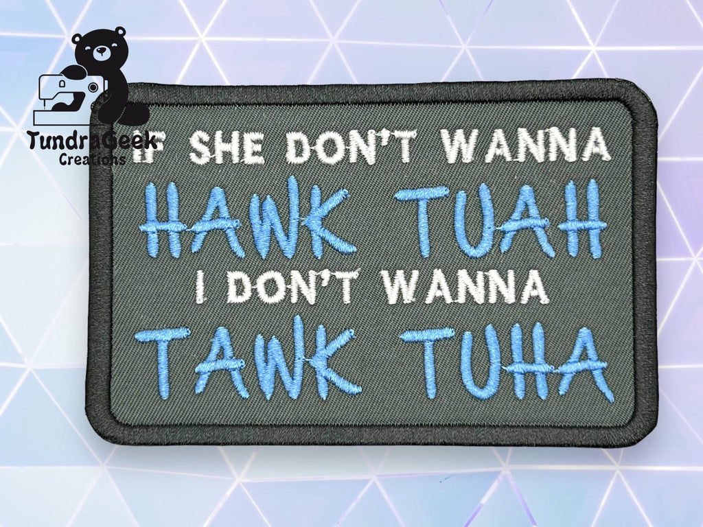 A fabric patch with the text: SHE DONT WANNA HANK TUAH I DONT WANNA TANK TUHA, on a gray background with a logo in the top left corner.