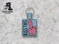 Embroidered keychain with a cartoon butt and the words KISS THIS on a gray background, with TundraGeek Creations logo in the top left corner.