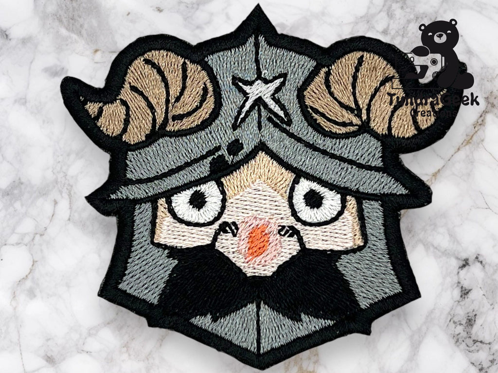 An embroidered patch depicts a cartoonish Viking with ram horns on a helmet, wide eyes, and a black beard. Marble surface background.