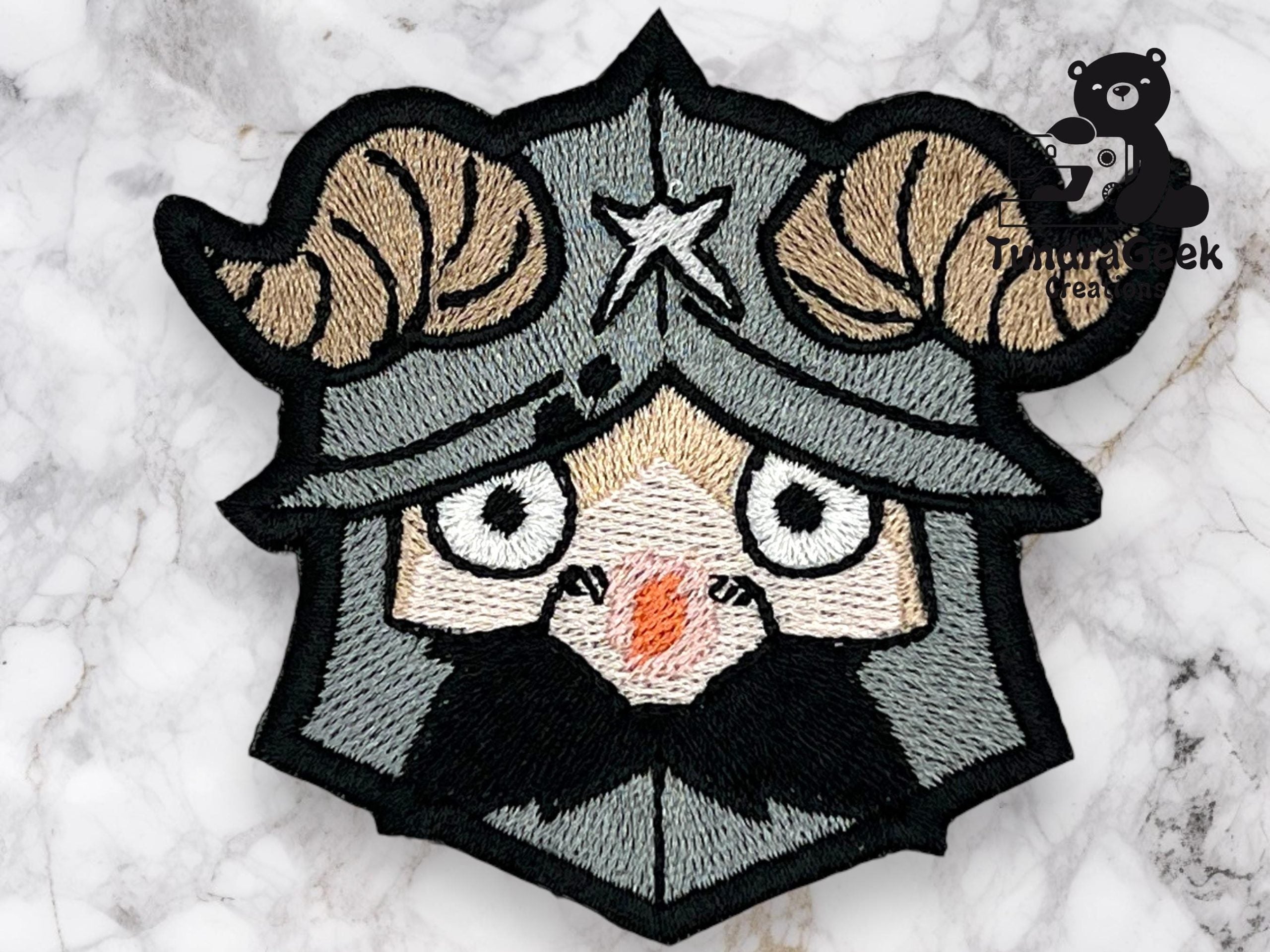 An embroidered patch depicts a cartoonish Viking with ram horns on a helmet, wide eyes, and a black beard. Marble surface background.