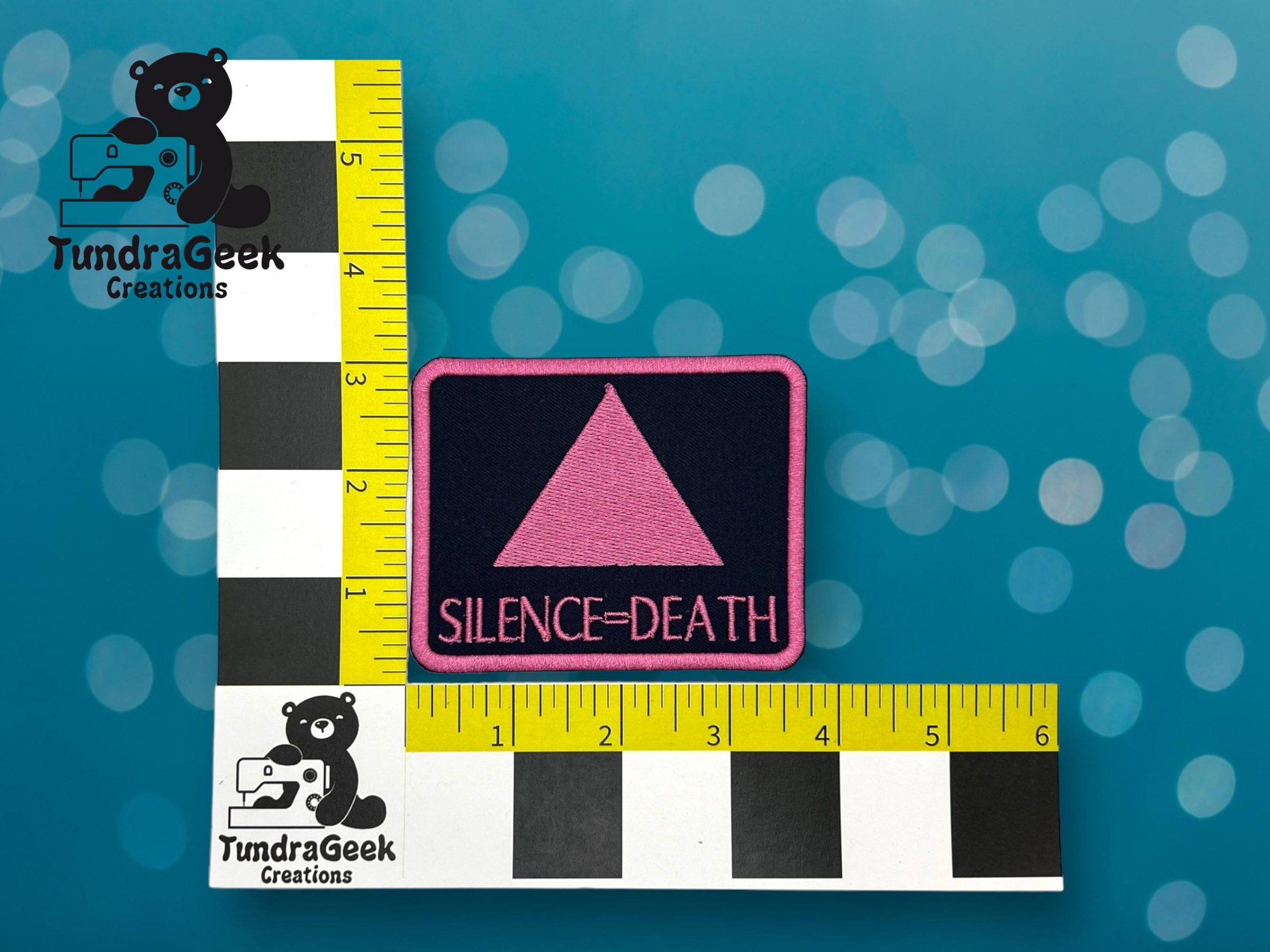 A rectangular patch with a pink triangle and the words SILENCE=DEATH on a black background, displayed on a measurement grid by TundraGeek Creations.