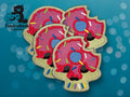 Four embroidered patches shaped like skulls with pink donut frosting and colorful sprinkles, shown on a blue background with the TundraGeek Creations logo in the corner.