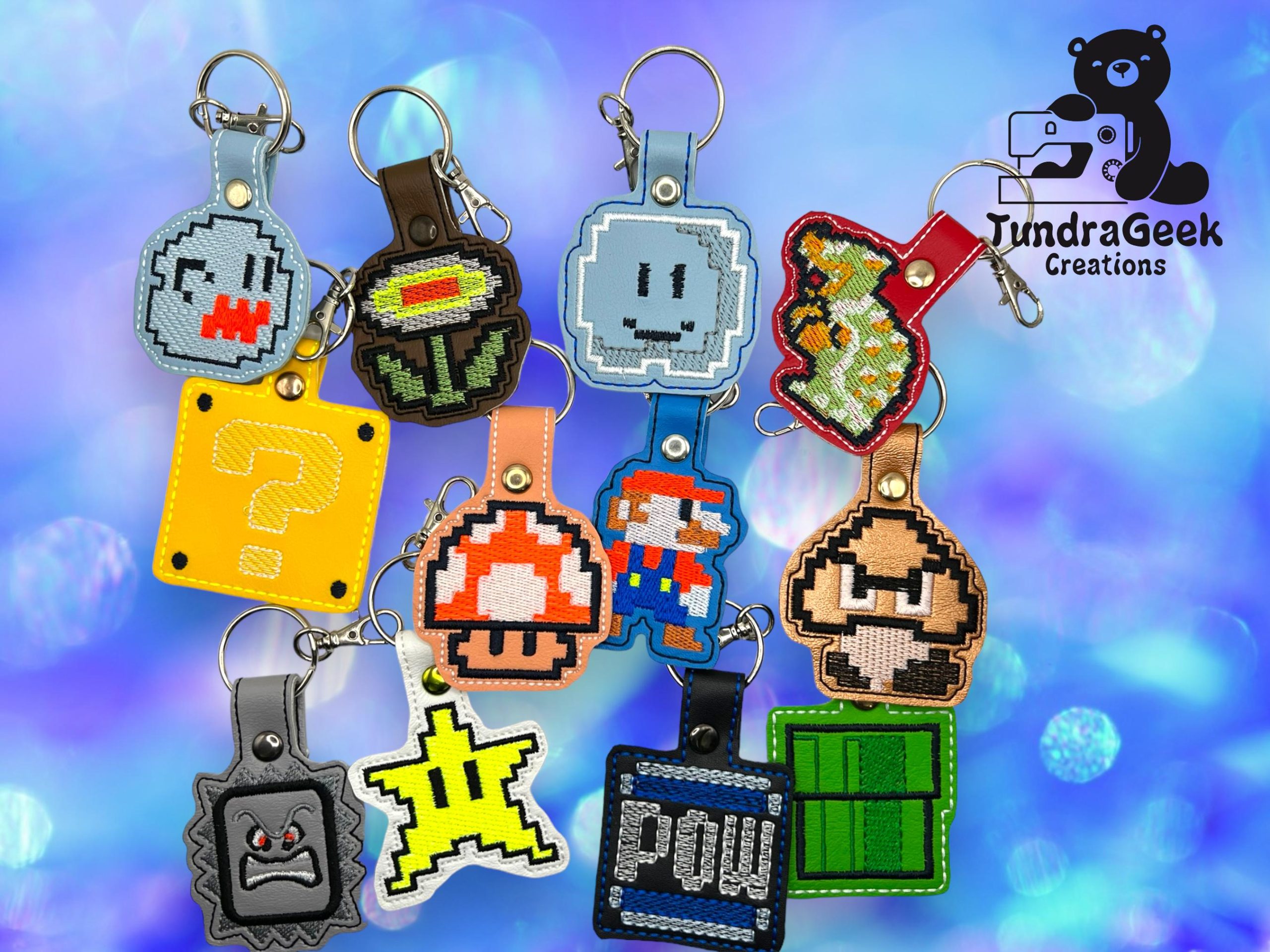 A collection of keychains featuring pixel art designs inspired by classic Mario game characters and items, displayed on a blue bokeh background with the TundraGeek Creations logo.