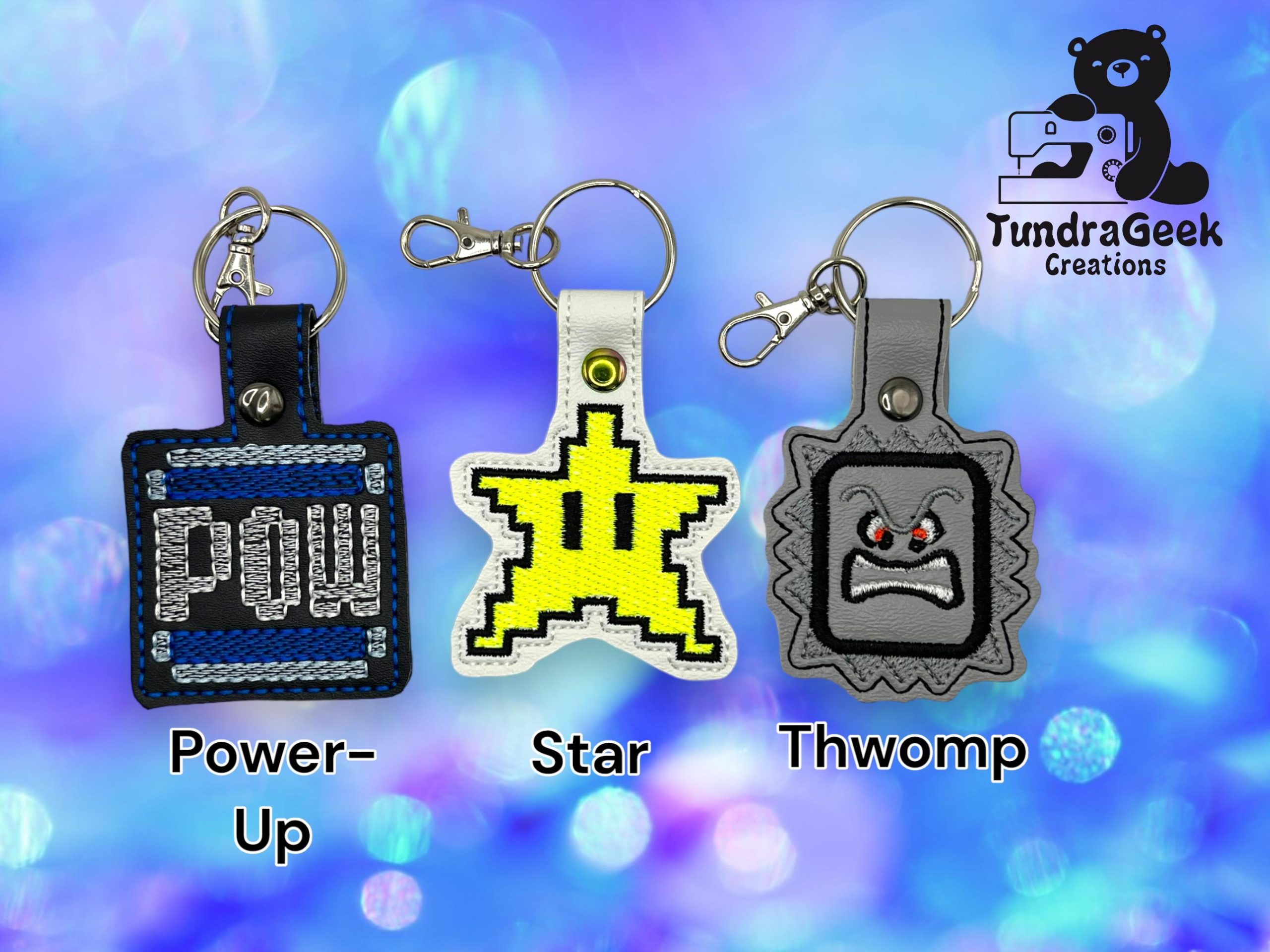 Three embroidered keychains labeled Power-Up, Star, and Thwomp, are displayed on a blue bokeh background with the TundraGeek Creations logo in the corner.