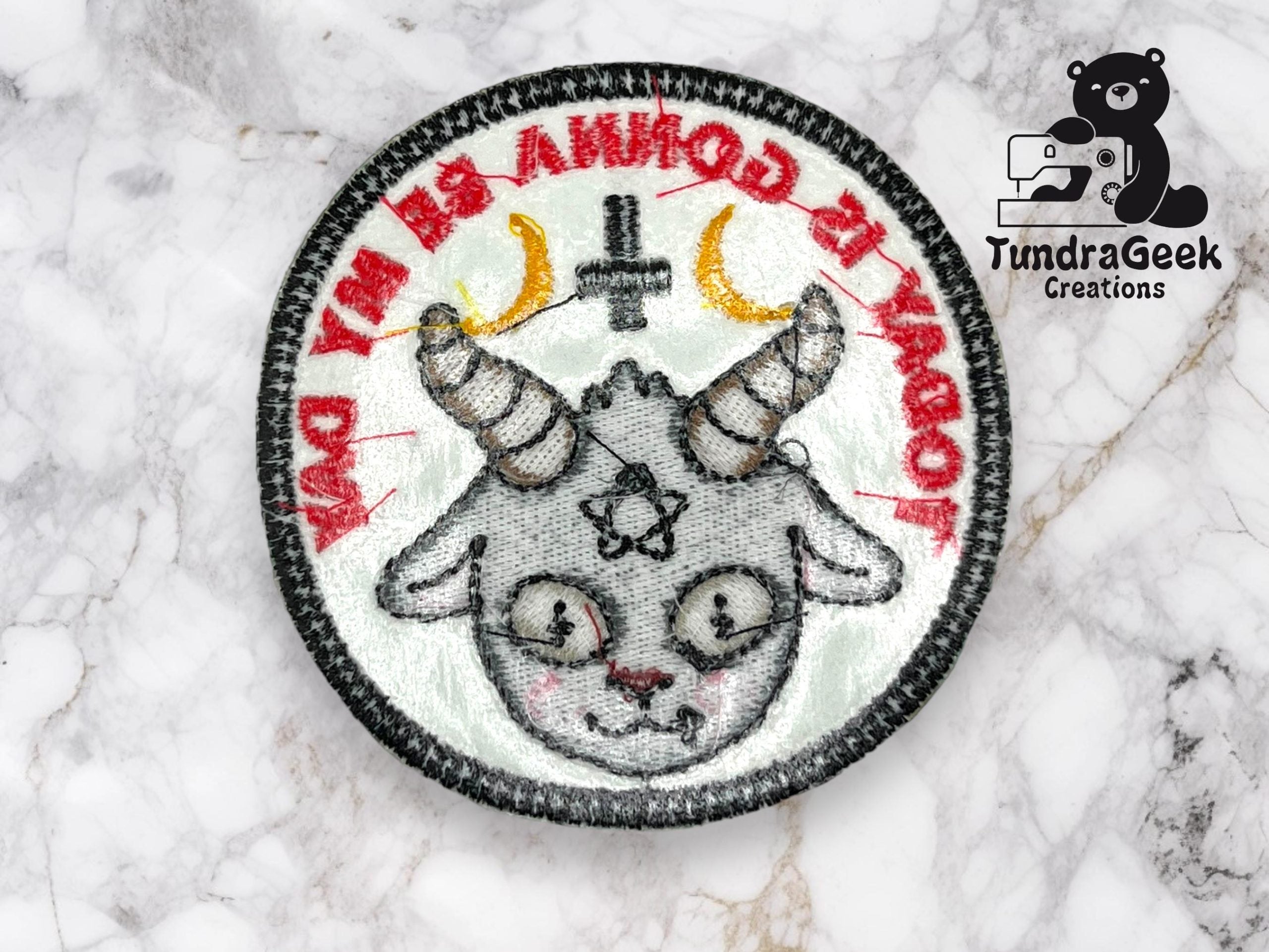 Embroidered patch featuring a cartoon goat with horns, crescent moons, and an inverted cross, with red text and TundraGeek Creations logo in the corner.
