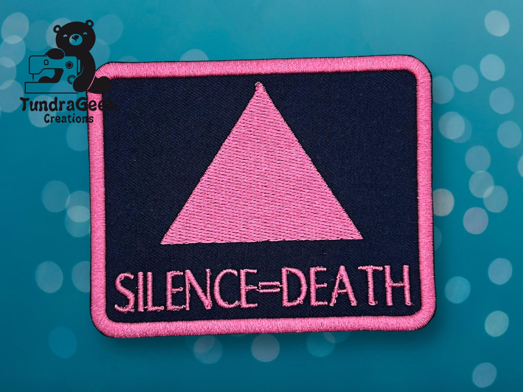 A rectangular patch with a pink triangle and the words SILENCE = DEATH in pink on a dark background, with the TundraGeek Creations logo in the upper left corner.