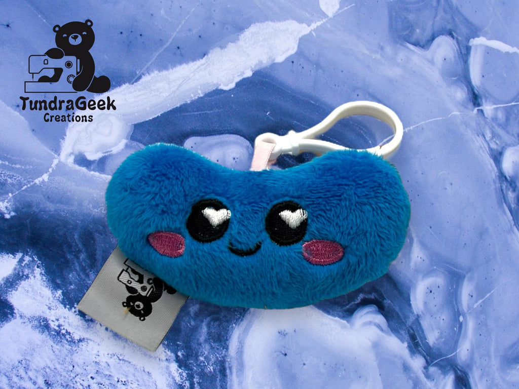 A blue plush keychain with a smiling face, heart-shaped eyes, and pink cheeks, displayed on a blue marbled background with the TundraGeek Creations logo.