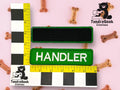 Two rectangular fabric patches, one blank and one labeled HANDLER, are placed next to measuring rulers on a pink surface with scattered dog bone treats. TundraGeek Creations logo appears twice.