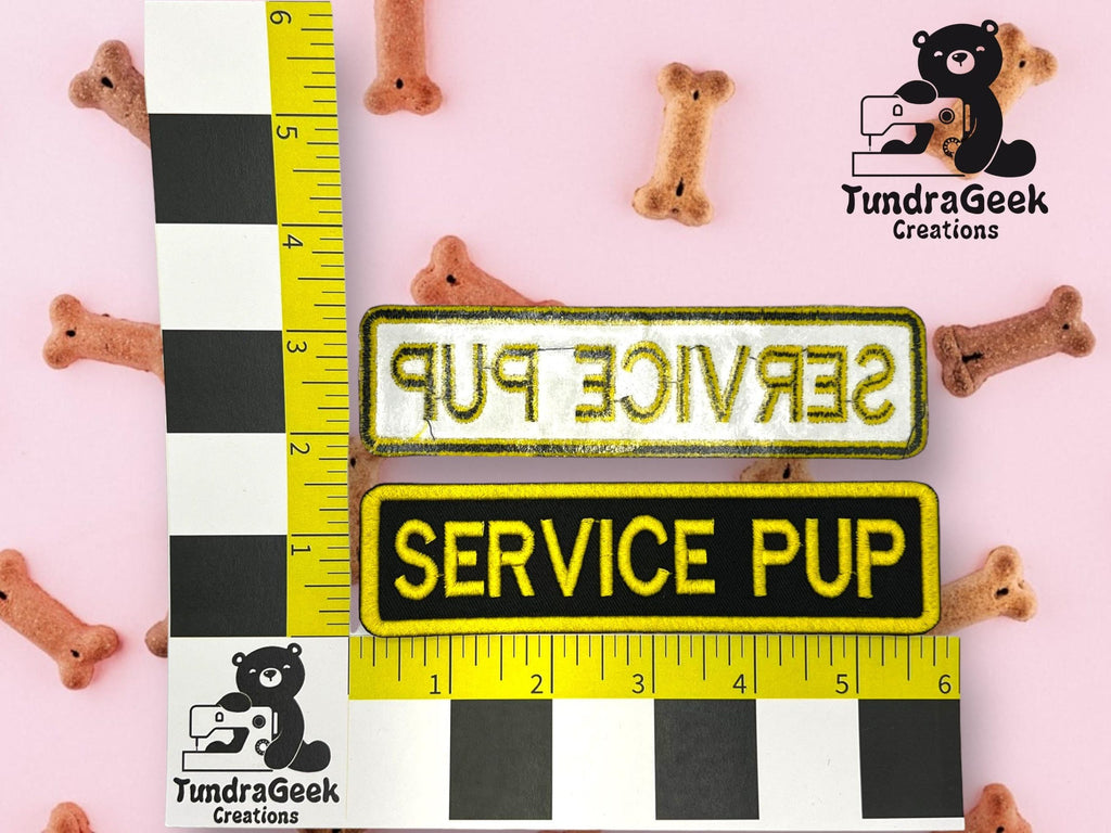 Two rectangular SERVICE PUP patches, one with a yellow border and one with a black border, are placed on a pink surface with dog bone treats and measurement rulers.