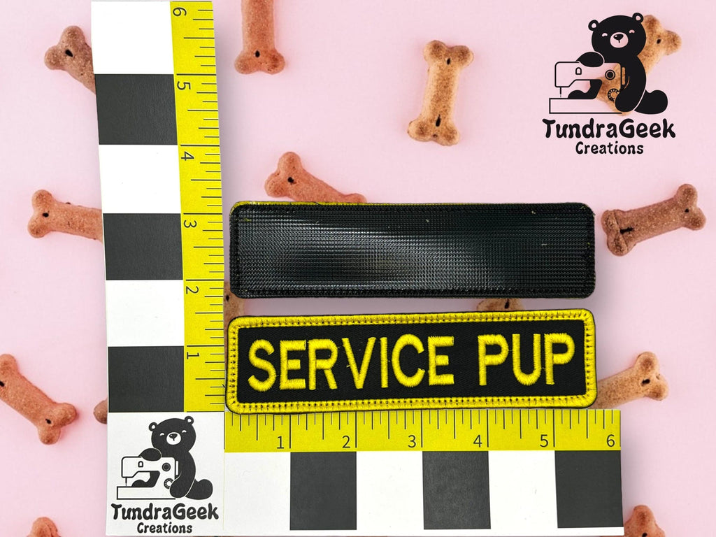 Two rectangular patches, one blank and one labeled SERVICE PUP, on a pink surface with dog bone treats and a yellow ruler for scale, TundraGeek Creations logo in corners.