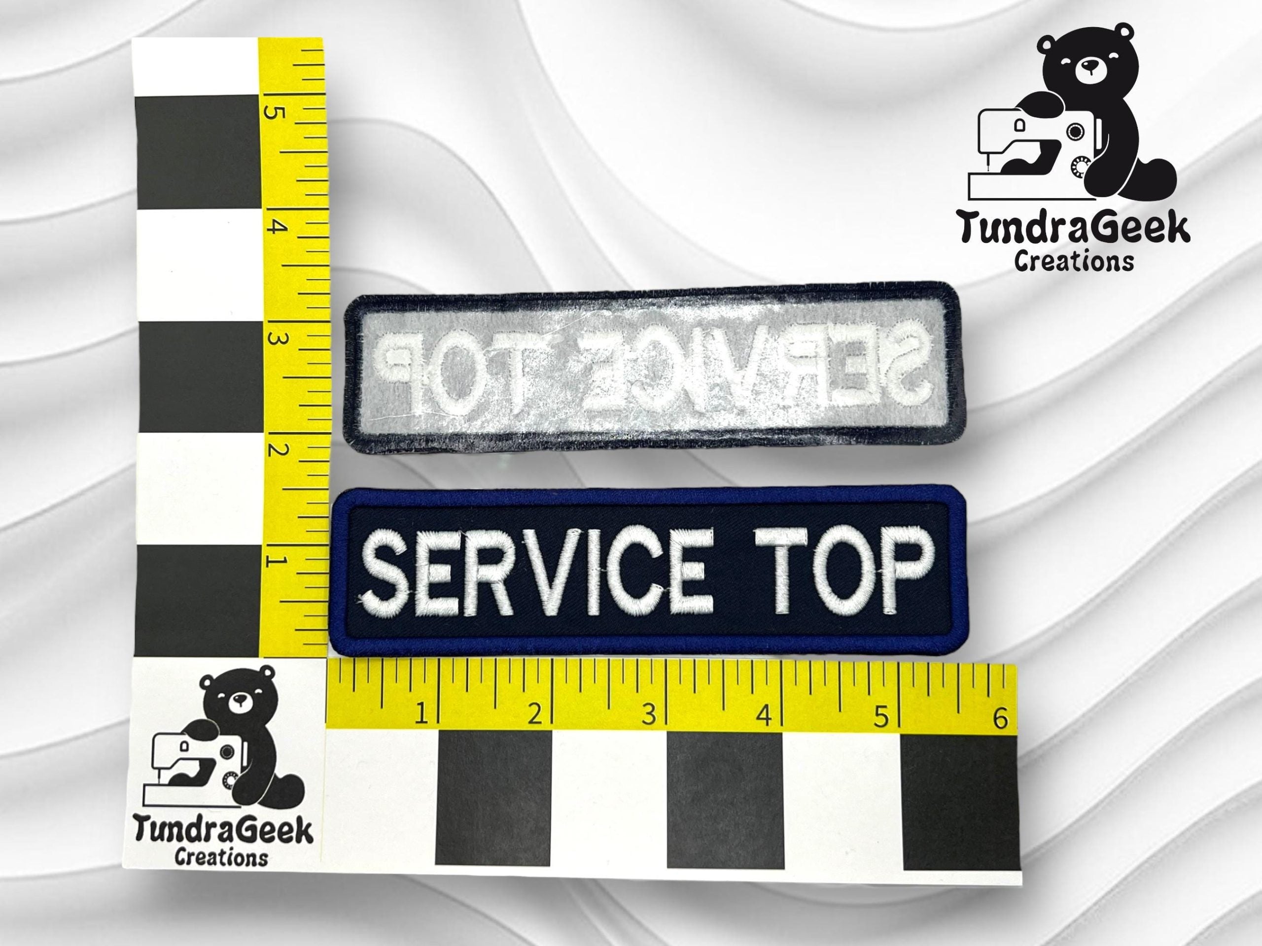Two rectangular patches with the text SERVICE TOP, one facing up with white text on blue and one facing down, beside rulers and the TundraGeek Creations logo featuring a bear with a sewing machine.
