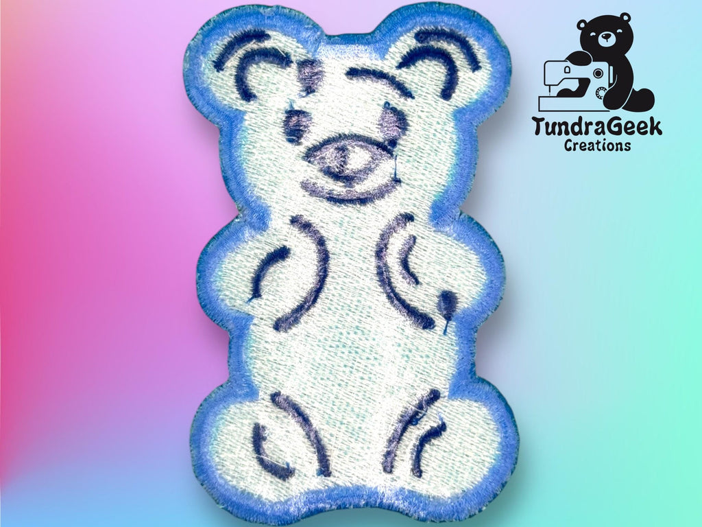 A blue and white stitched bear patch is displayed on a pastel gradient background, with the TundraGeek Creations logo in the top right corner.