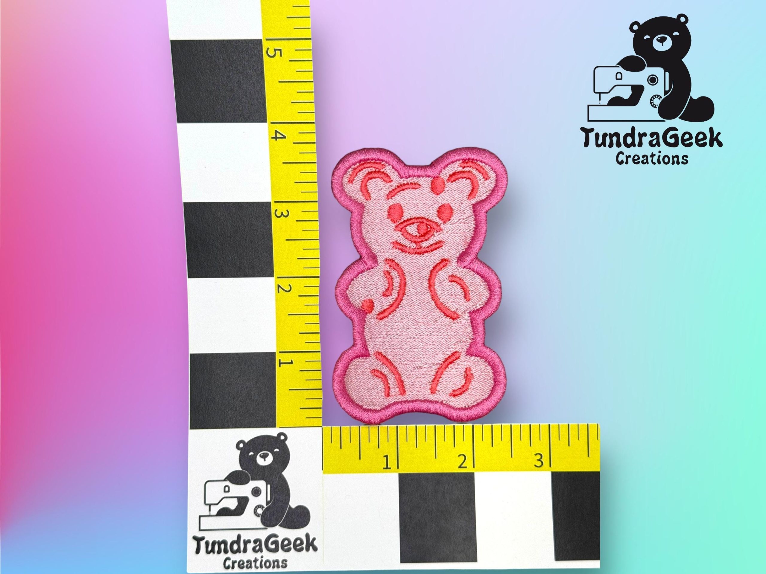 A pink embroidered bear patch is placed next to a yellow ruler showing it measures about 2.5 inches tall. TundraGeek Creations logo appears in two corners.