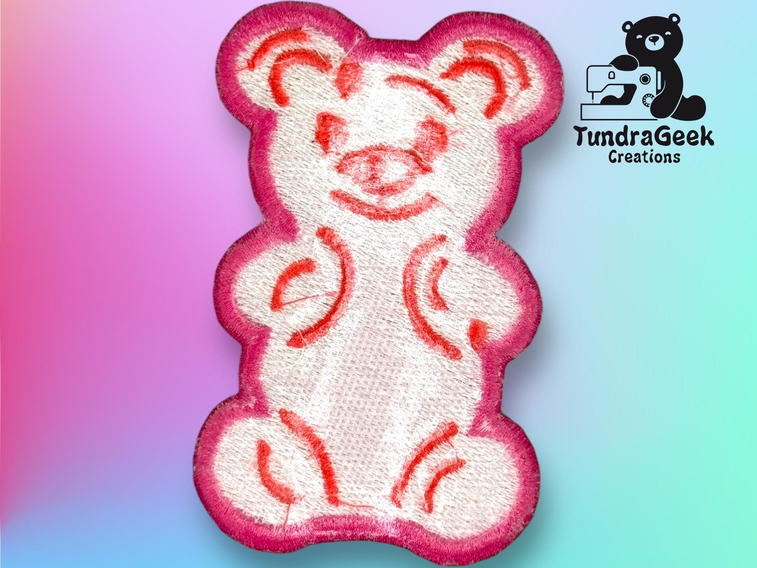 Embroidered patch of a simple bear outline in white with pink border and orange details, displayed on a pastel gradient background with the TundraGeek Creations logo in the corner.
