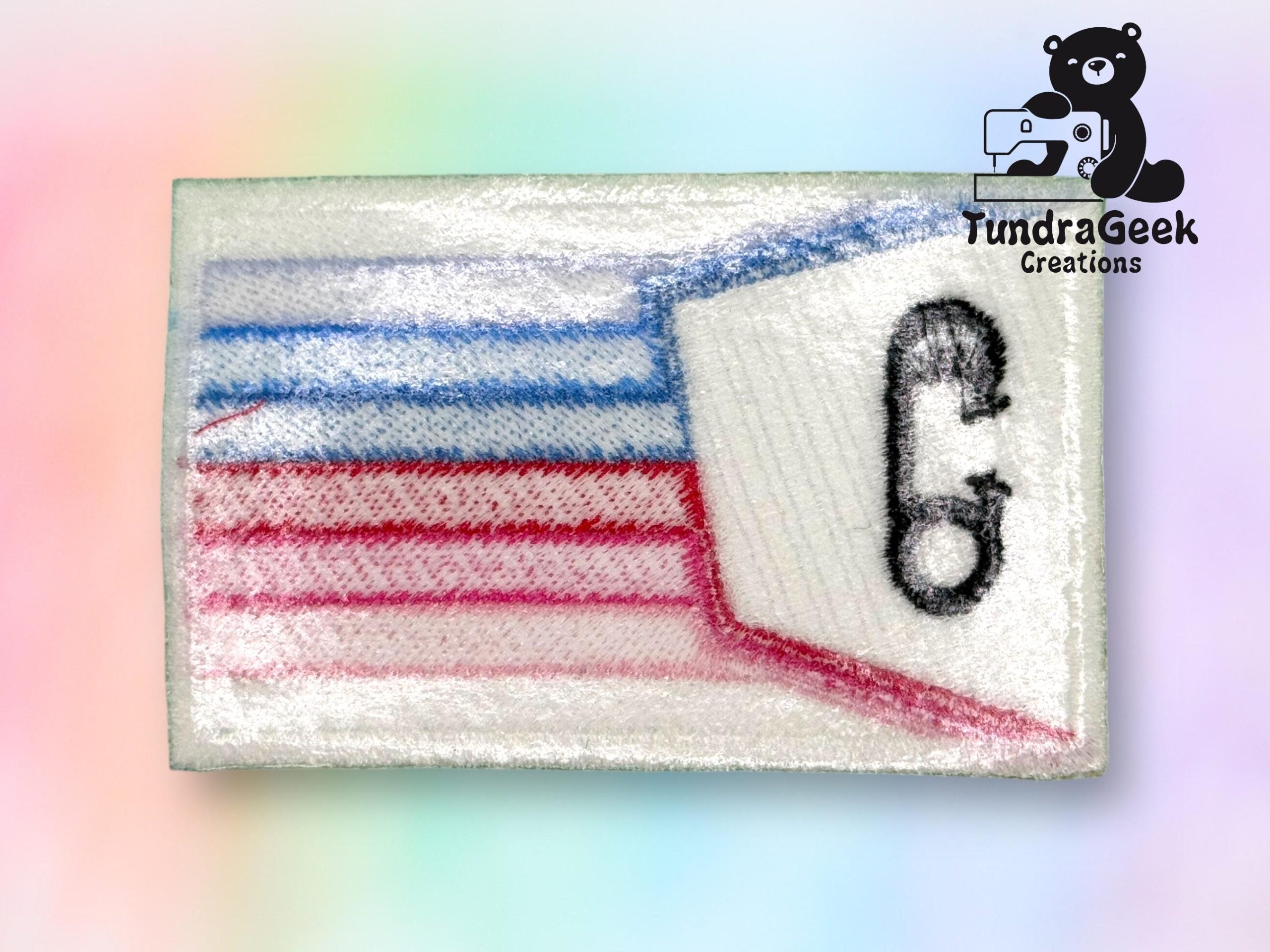 Rectangular embroidered patch with blue and red lines, a stylized phone icon, and a TundraGeek Creations logo featuring a bear with a sewing machine in the top right corner.