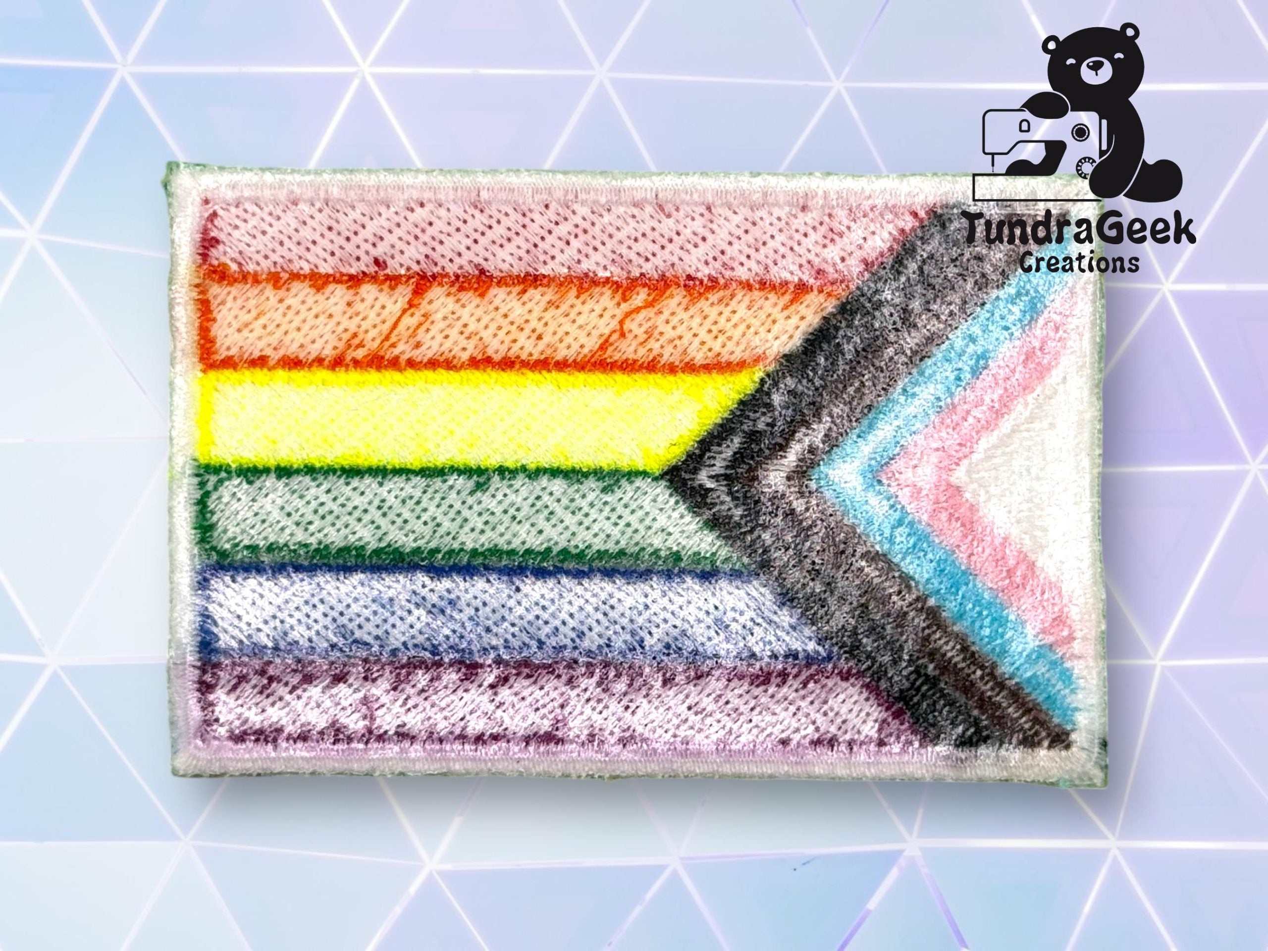 A Progress Pride flag patch displayed on a geometric light blue background with a black bear and TundraGeek Creations logo in the top right corner.