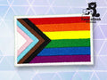 Rectangular embroidered patch featuring the Progress Pride flag with rainbow stripes and a chevron of white, pink, blue, brown, and black. TundraGeek Creations logo in the top right corner.