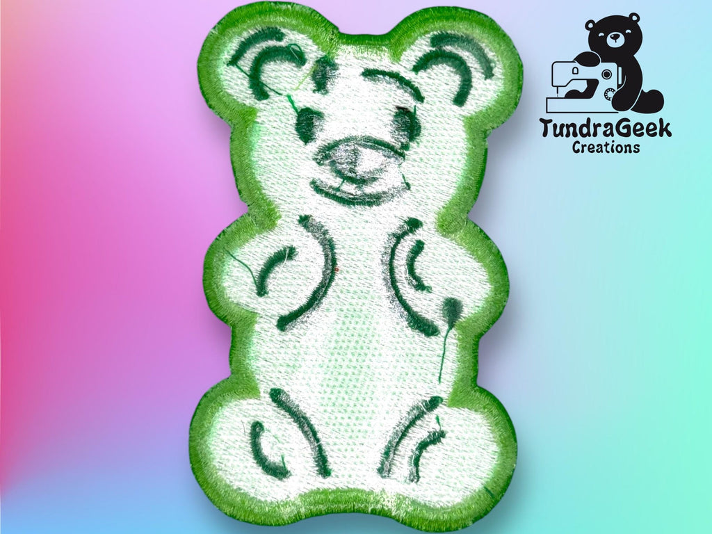 Embroidered patch of a white teddy bear outlined in green on a gradient background, with the TundraGeek Creations logo in the top right corner.