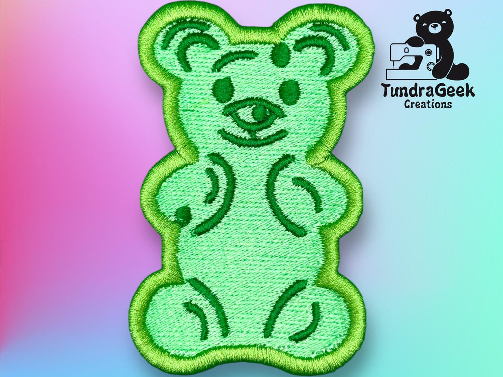 Green embroidered patch of a teddy bear on a pastel gradient background, with the TundraGeek Creations logo featuring a bear and sewing machine in the top right corner.