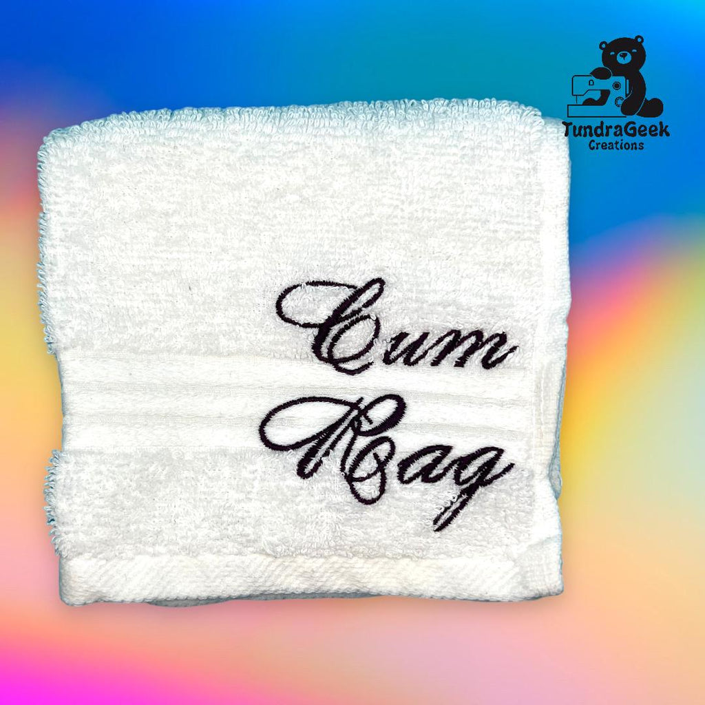 A white towel with the words Cum Rag embroidered in black script, displayed on a colorful gradient background with a TundraGeek Creations logo.