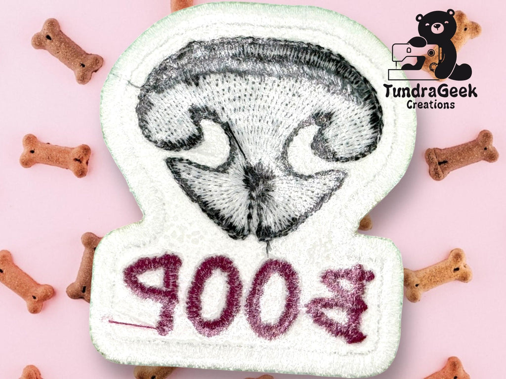 Embroidered patch of a dogs nose with “B00P” stitched upside down, surrounded by dog bone treats on a pink background. TundraGeek Creations logo in the top right corner.
