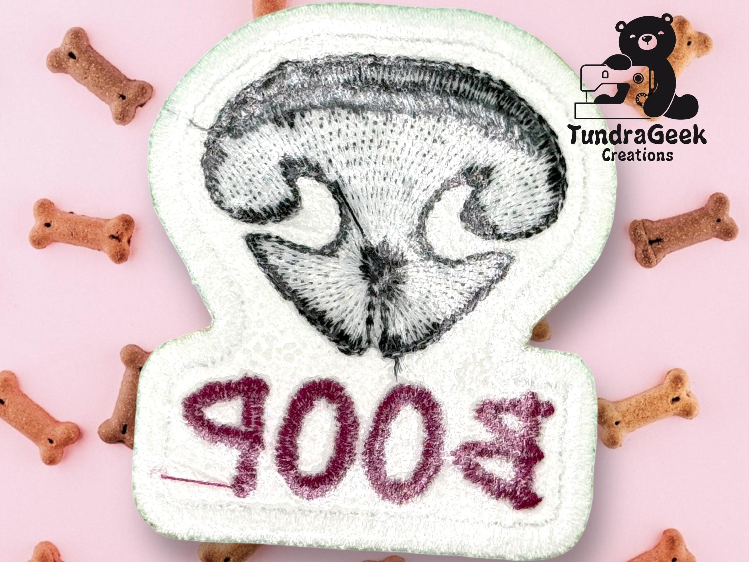 Embroidered patch of a dogs nose with “B00P” stitched upside down, surrounded by dog bone treats on a pink background. TundraGeek Creations logo in the top right corner.