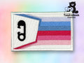 A rectangular embroidered patch features the they/them pronoun in lowercase letters on a white background with blue, purple, and pink stripes. The TundraGeek Creations logo appears in the top right corner.